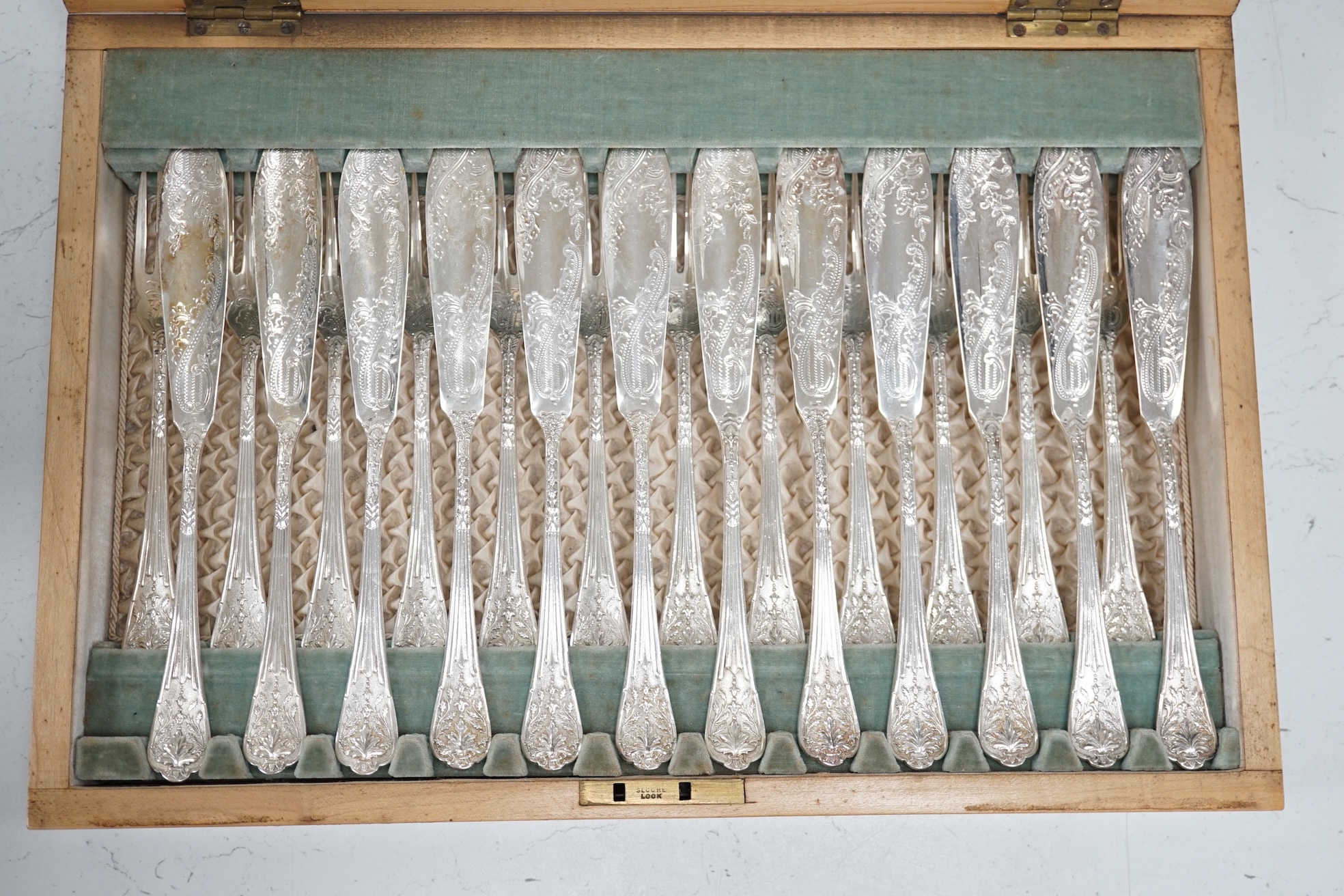 A set of twelve plated and engraved fish knives and forks, together with a pair of servers, housed in a mahogany case, 39cm wide. Condition - fair to good